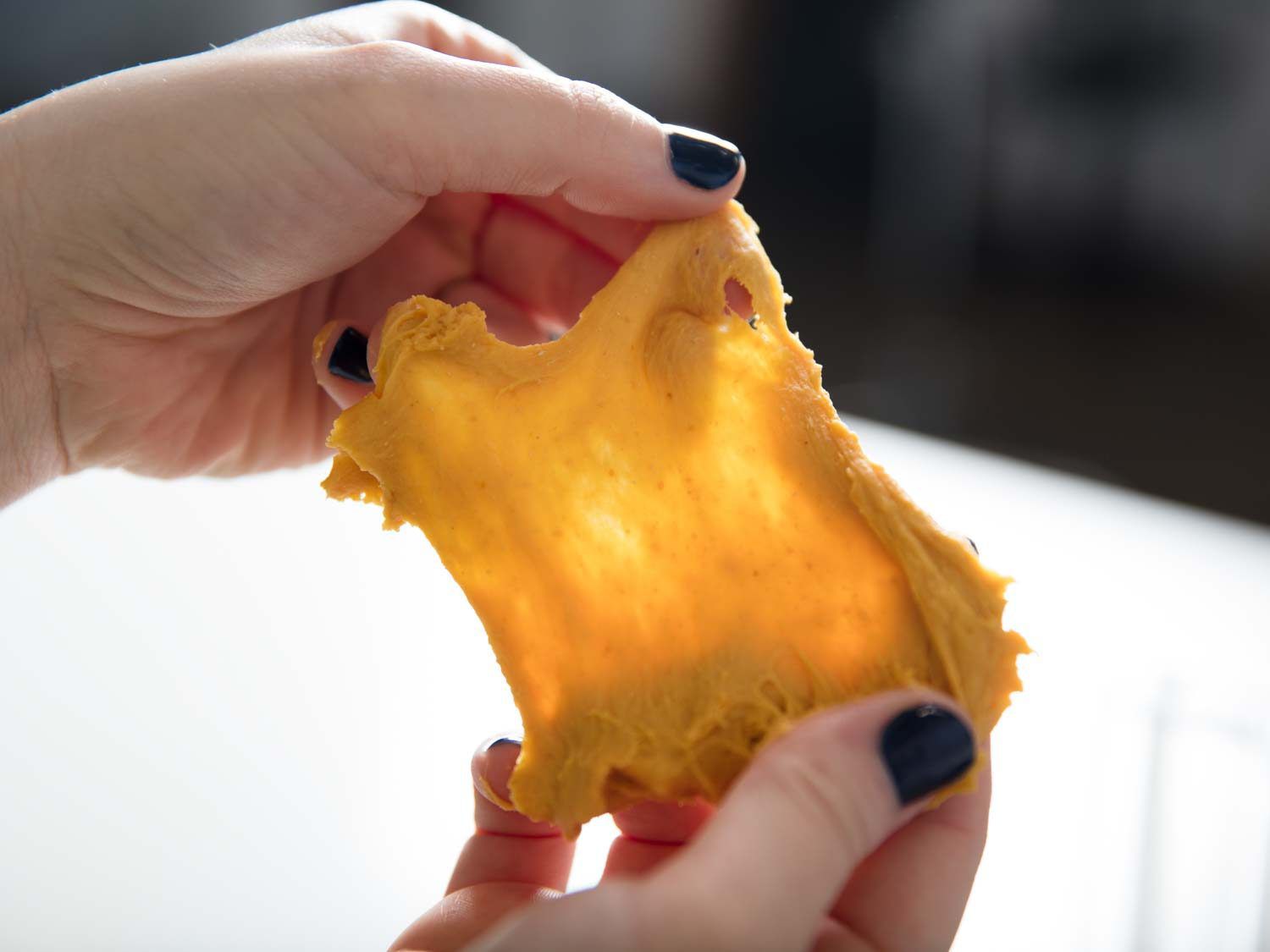 Hands using the windowpane test to see if dough for pumpkin sandwich bread has developed enough gluten.