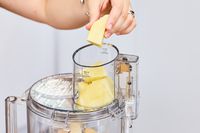 A person places parmesan cheese into the top of the Cuisinart 14-Cup Food Processor