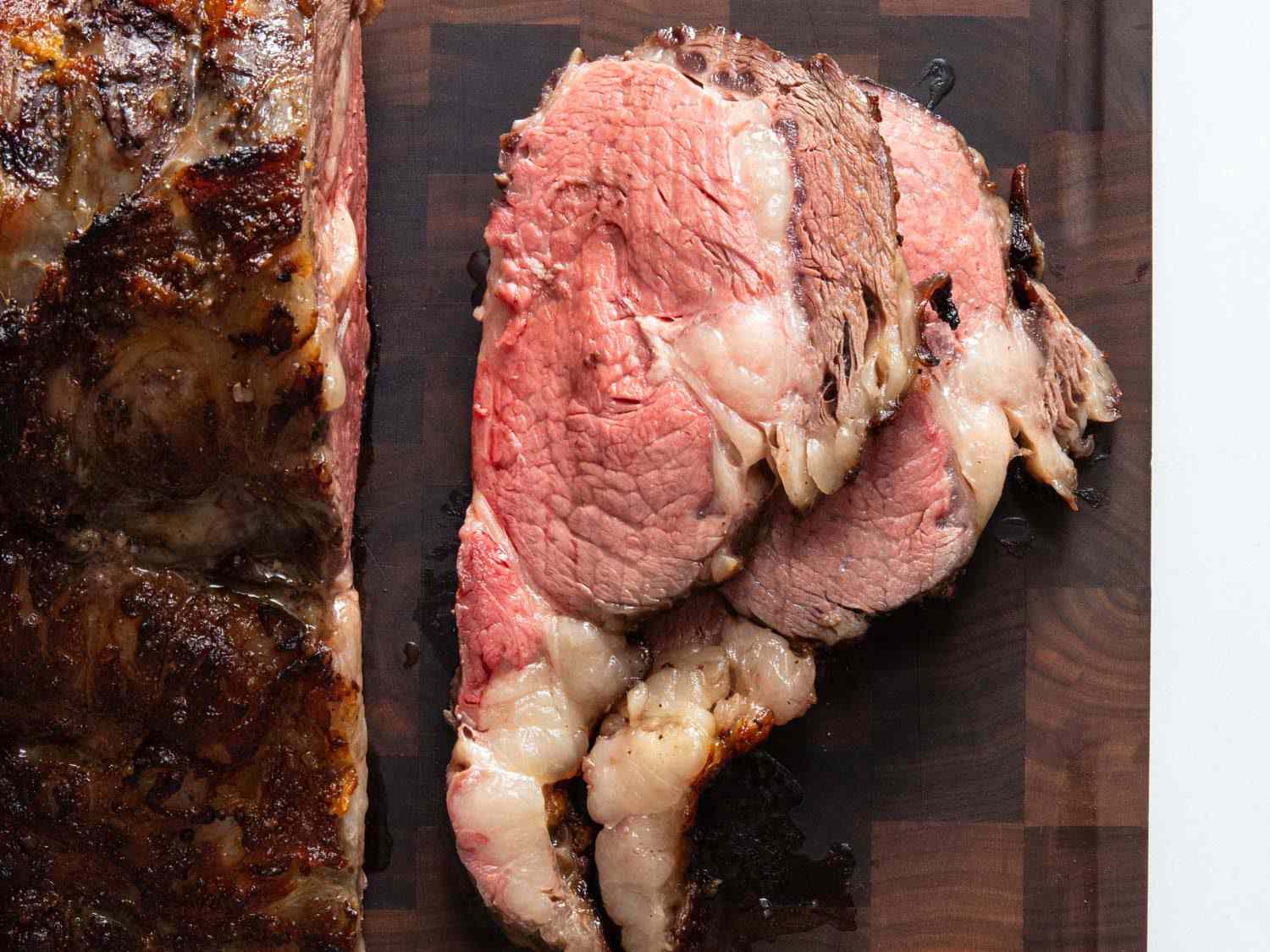 Closeup overhead of two thick slices of koji prime rib on a carving board with the remaining unsliced prime rib.