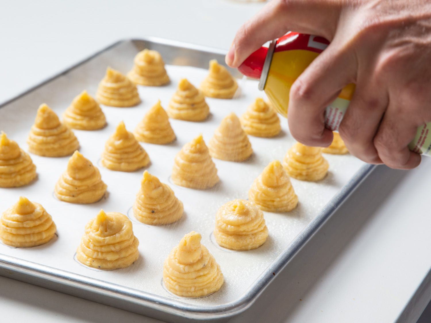 Nonstick cooking spray is applied to the choux paste mounds.