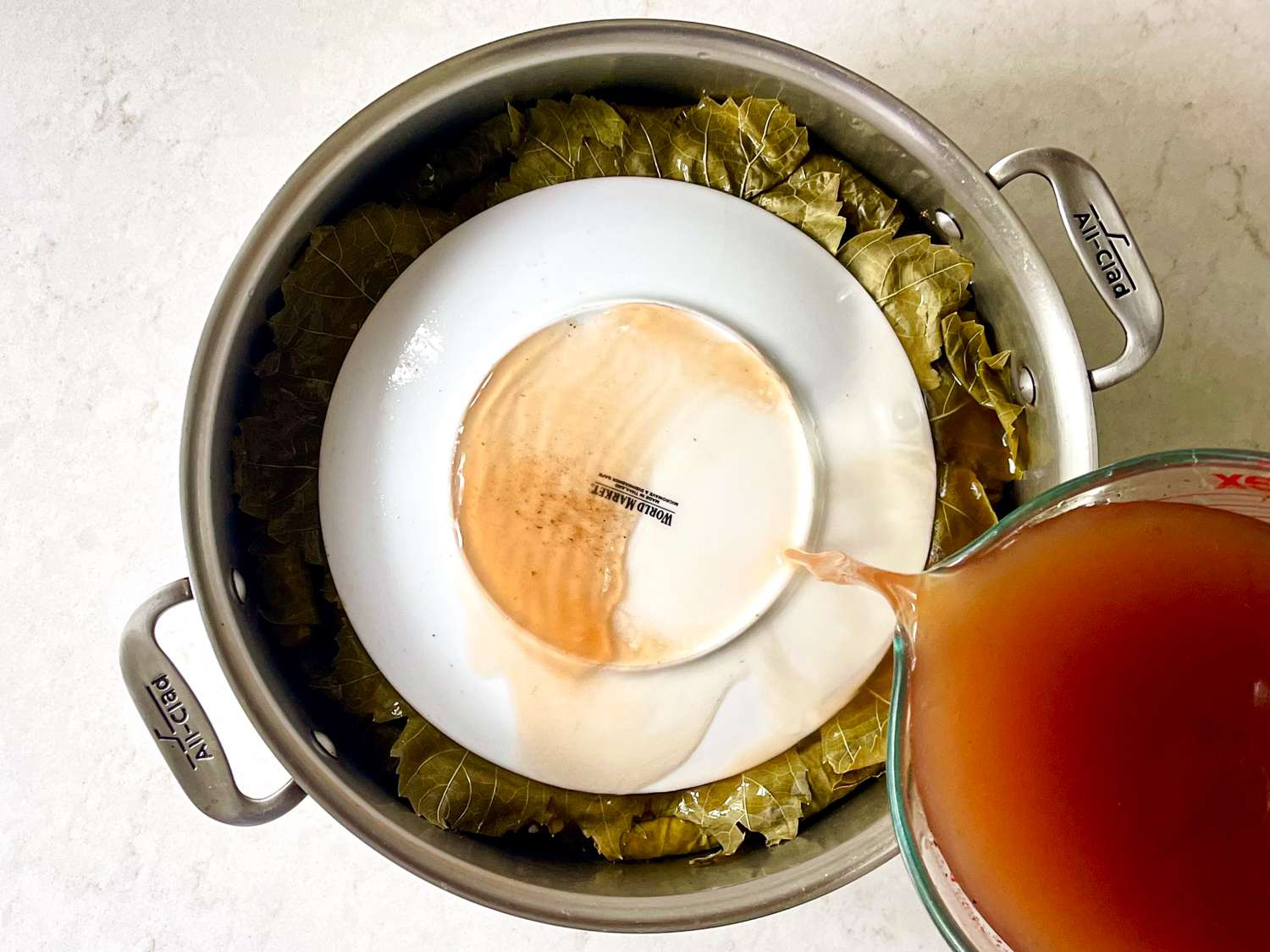 Broth being poured over and inverted plate placed ontop of grape leaves