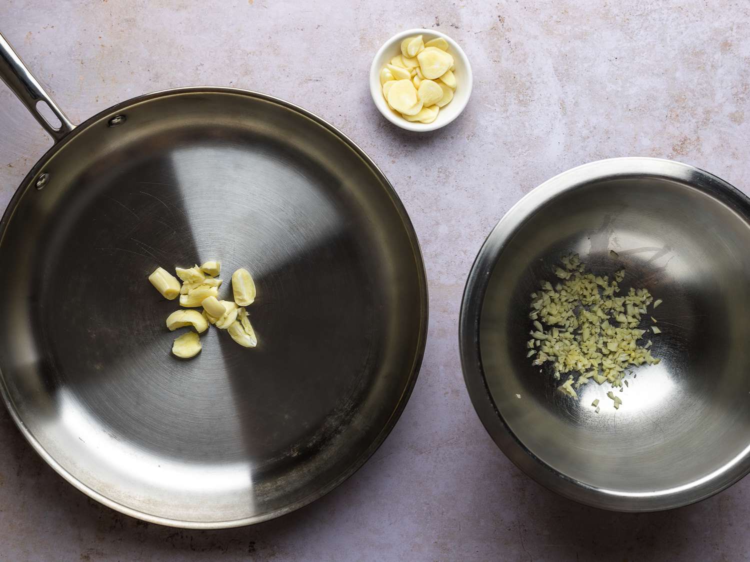 Finely minced garlic inside a large bowl, smashed garlic in a large skillet (off heat), and thinly sliced garlic in a small prep bowl.