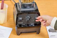 A close-up of a hand flipping a switch on the Vitamix E310 Explorian Blender