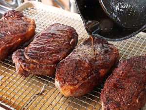 Hot pan drippings are poured on seared and rested steaks to "fat flash" them.