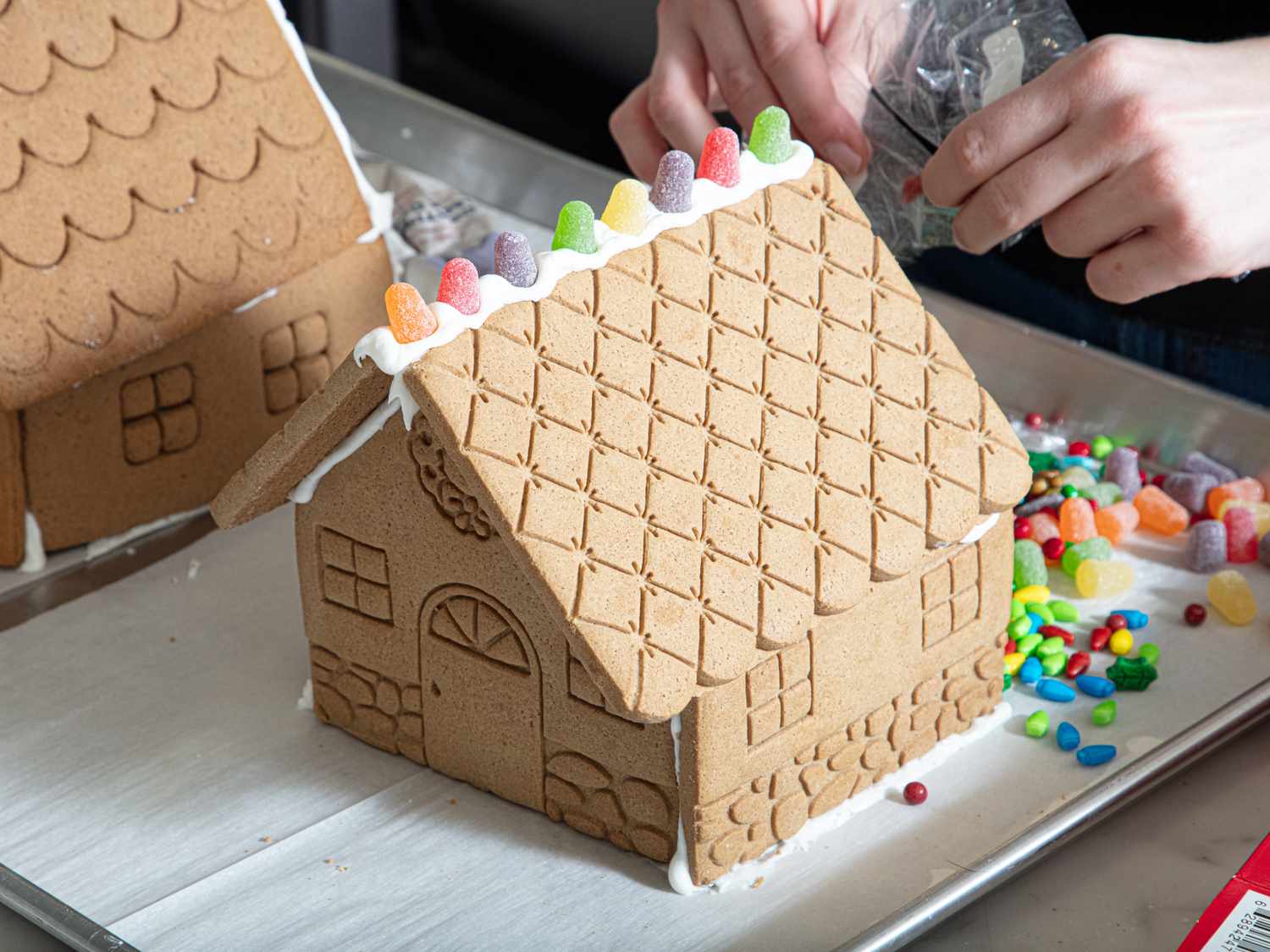Decorating a gingerbread house with candy gummies on the roof