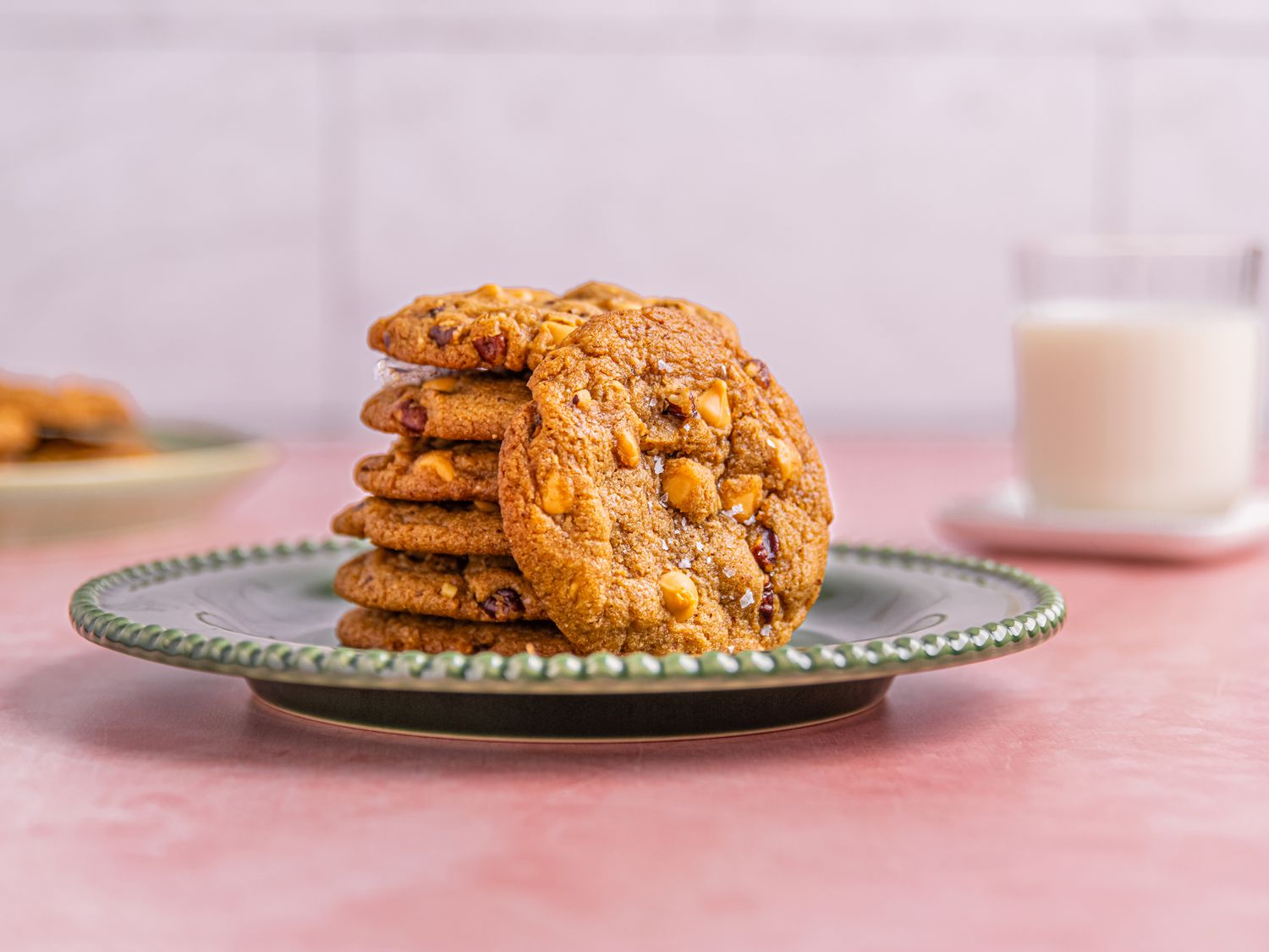 A plate of cookies, stacked with a glass of milk in the background
