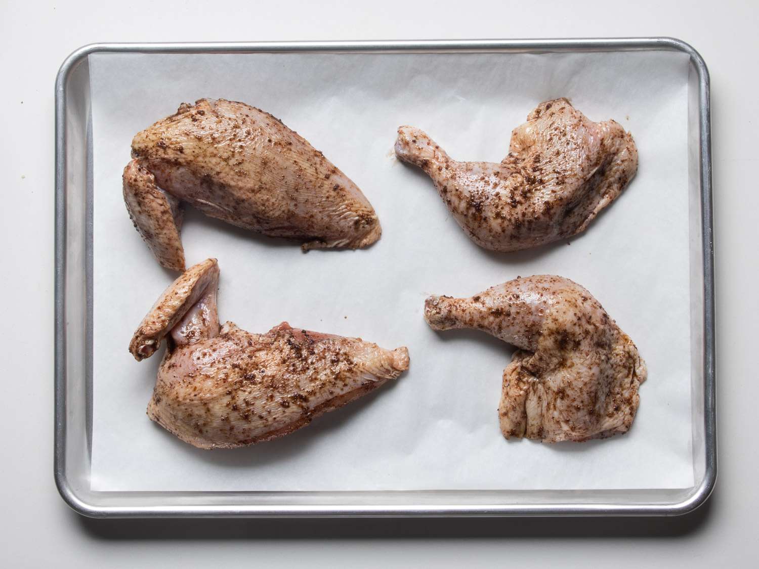 Seasoned chicken on a parchment-lined baking sheet.
