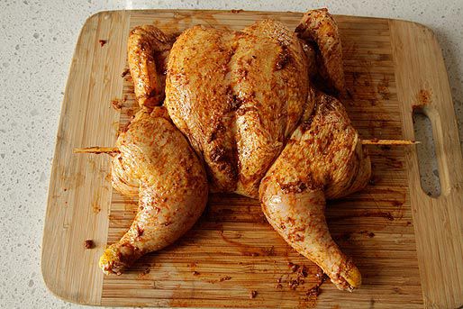 A spatchcocked chicken held in place with a skewer and rubbed with spice mixture for Peruvian grilled chicken.
