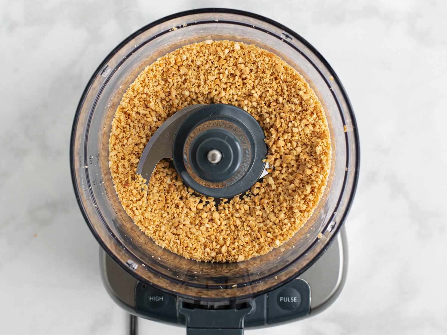 Peanuts and sugar pulsed into a coarse powder inside of a food processor bowl.