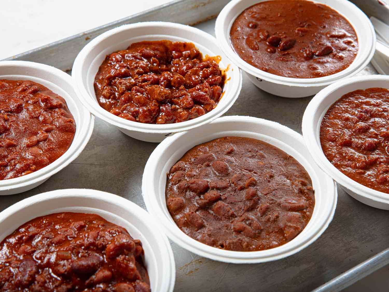 Several cups of chili arranged on a surface displaying varied textures and compositions