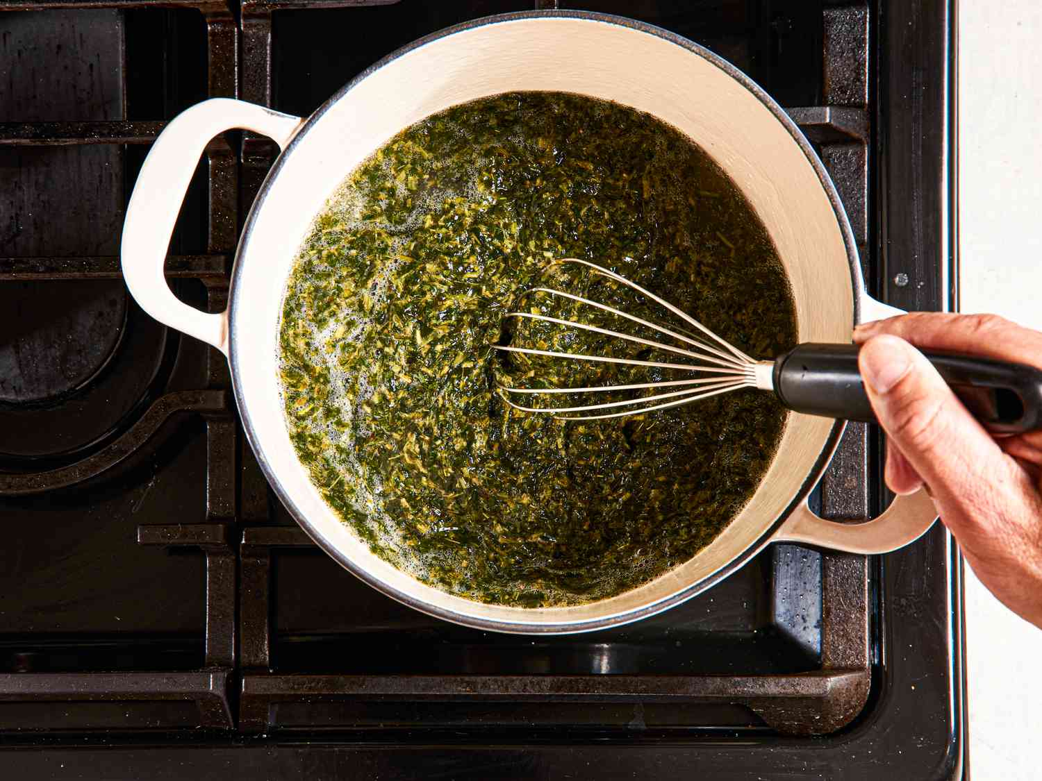 Whisking molokhia into chicken broth in a Dutch oven.