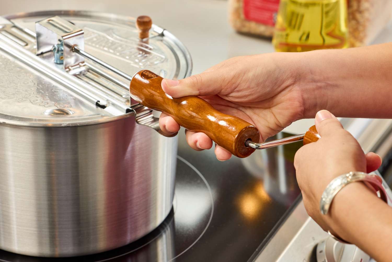 A person turns a crank on the Wabash Valley Farms Original Whirley-Pop Popcorn Popper Stainless Steel handle