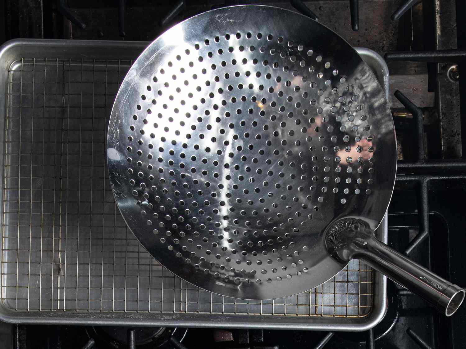 A perforated skimmer resting on top of a stove