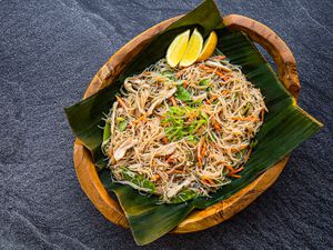 Overhead view of pancit bihon, served in a wooden bowl that has been lined with a square of banana leaf.
