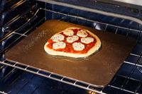 A pizza topped with mozzarella cheese and tomato sauce on a baking steel in the oven.