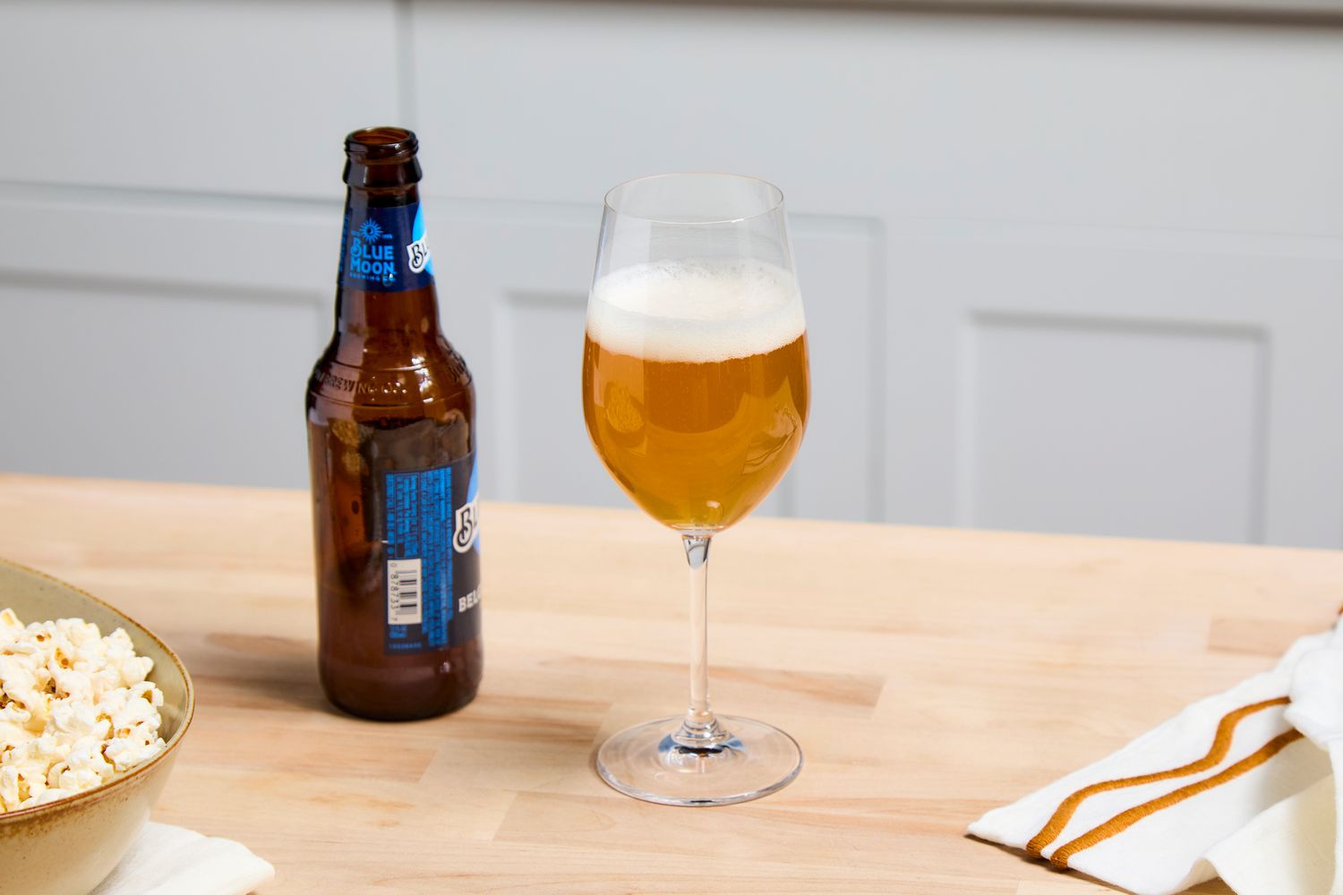 A wine glass filled with beer. A bottle of beer is beside it. 
