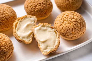 Six choux au craquelins on a white platter with one of them cut in half.