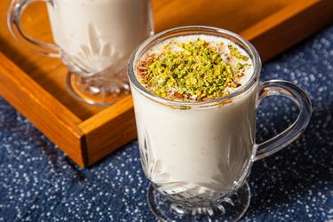 Two glasses of sahlab topped with pistachios and spices on a tray