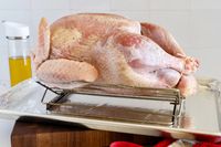 Raw turkey on roasting rack oil bottle in background