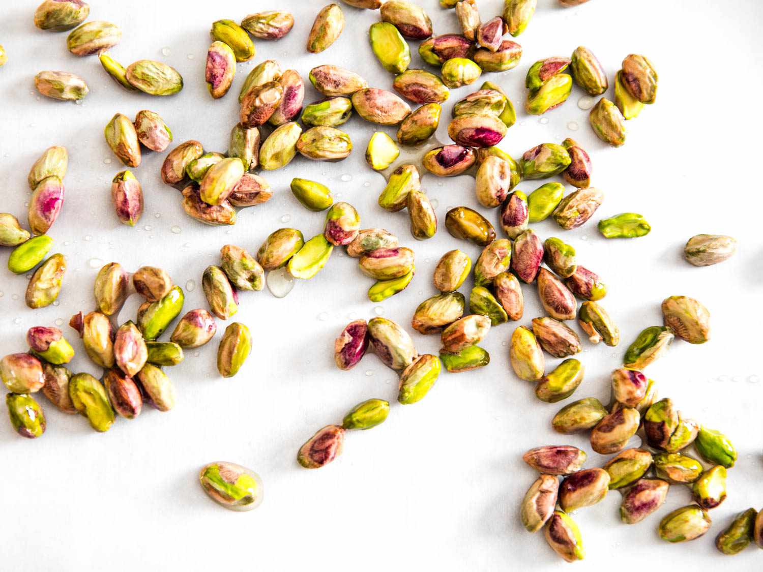 A bunch of candied pistachios, scattered on a white background.