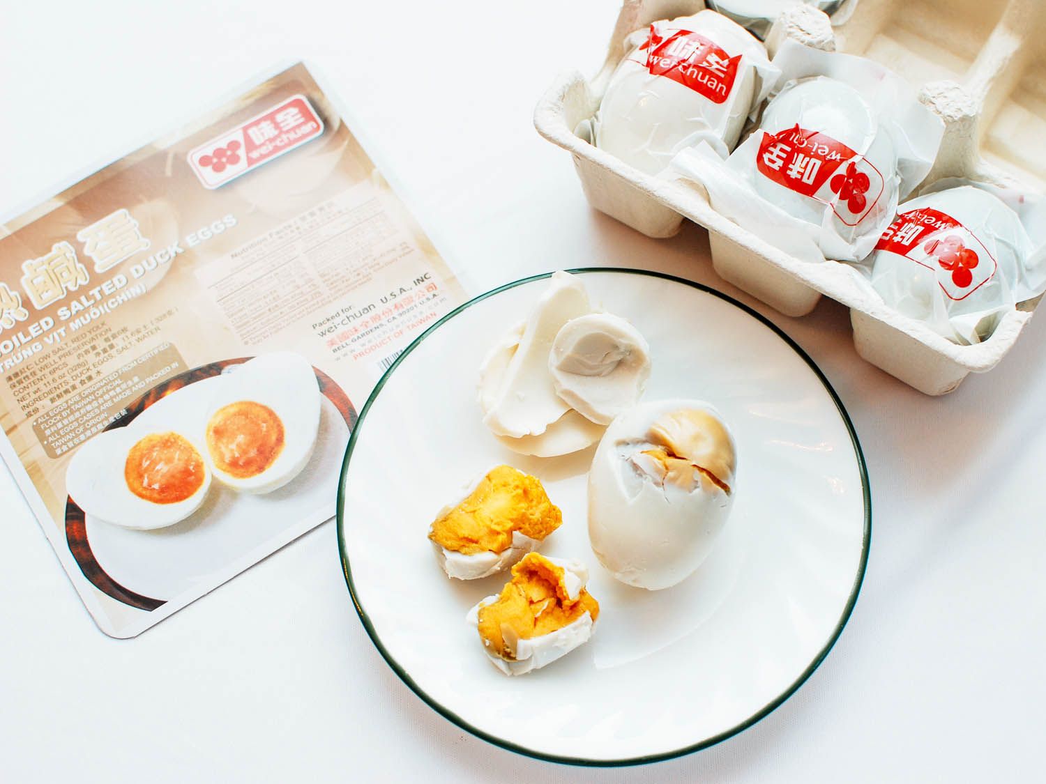 A ceramic plate with a peeled salted egg on it, with more salted eggs in packaging on the periphery.