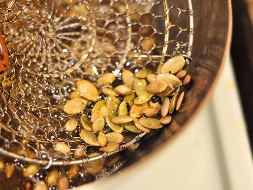Almonds, peanuts, pumpkin seeds, and raisins being fried in oil.