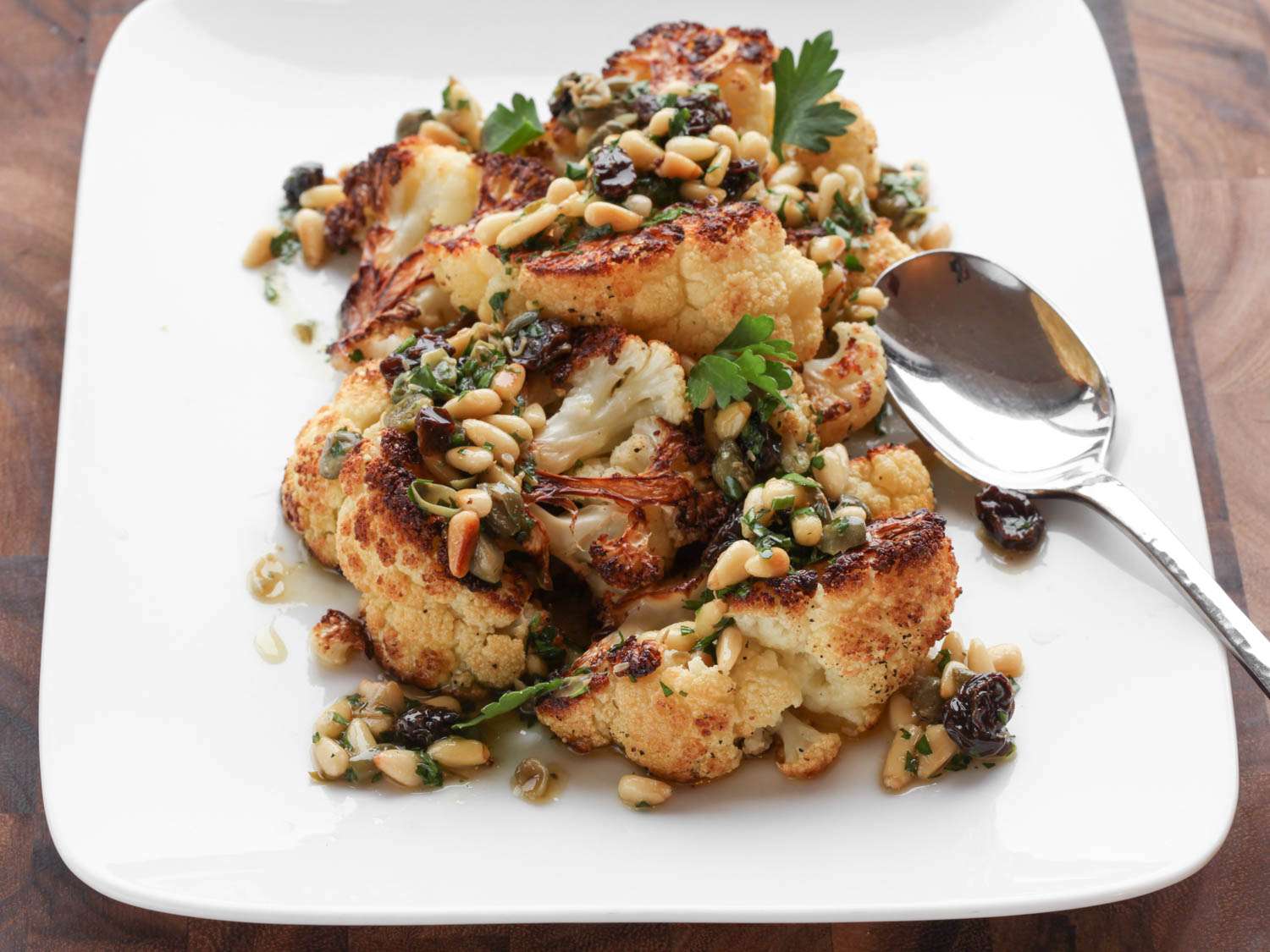 Roasted Cauliflower With Pine Nut, Raisin, and Caper Vinaigrette, served on a square white plate.