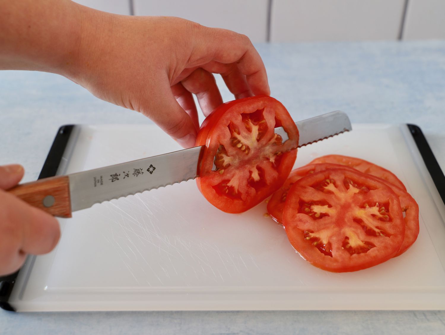 Hands slicing tomatoes with the Tojiro F-737 Bread Slicer