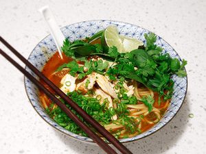  A bowl of Thai Red Curry Noodle Soup With Chicken, with soup spoon and chopsticks.