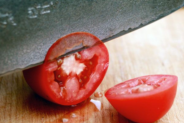 Close-up of a knife slicing a tomato on a wooden surface