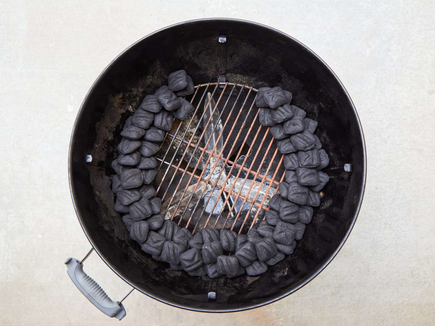 Circular barbecue grill with charcoal arranged around the perimeter and a small fire in the center