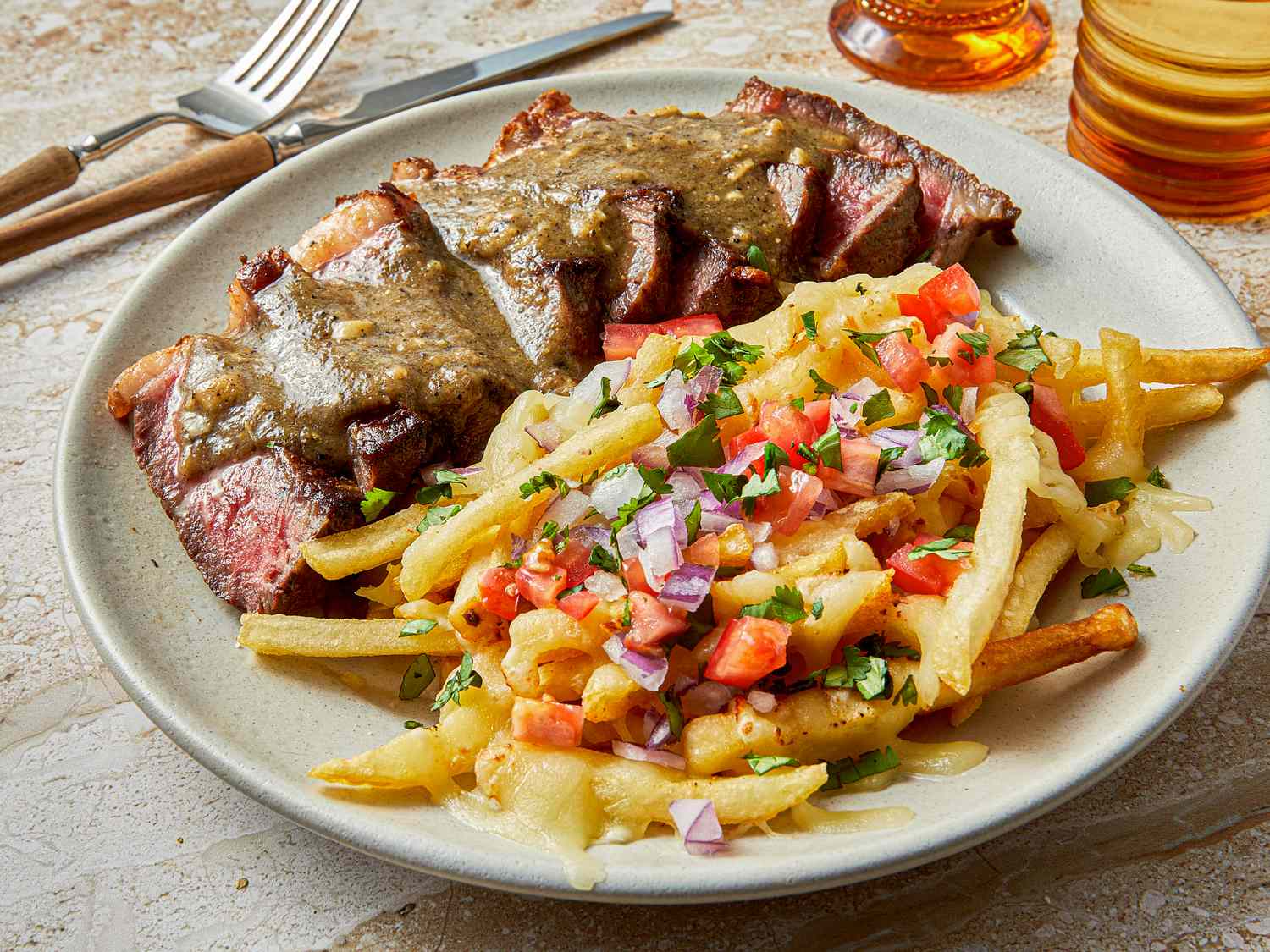 A plate of carne asada fries topped with pico de gallo next to slices of grilled steak covered in sauce served on a table