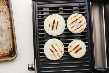 Onions cooking on an indoor grill next to a sheet pan