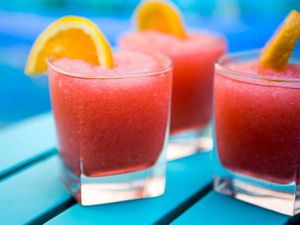a profile view of a rocks glass filled with red frozen negroni, garnished with an orange wedge