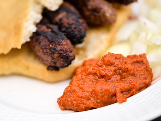 A dollop of ajvar on a plate, flanked by a cevapi sandwich.