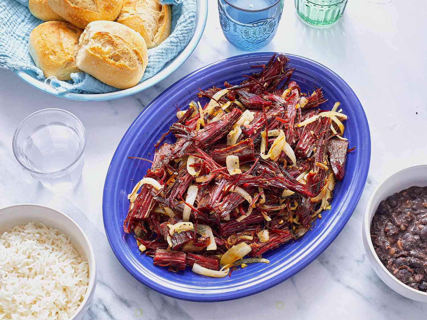 Tasajo on blue platter, with sides of rice and beans and plate of biscuits and glasses of water to the side