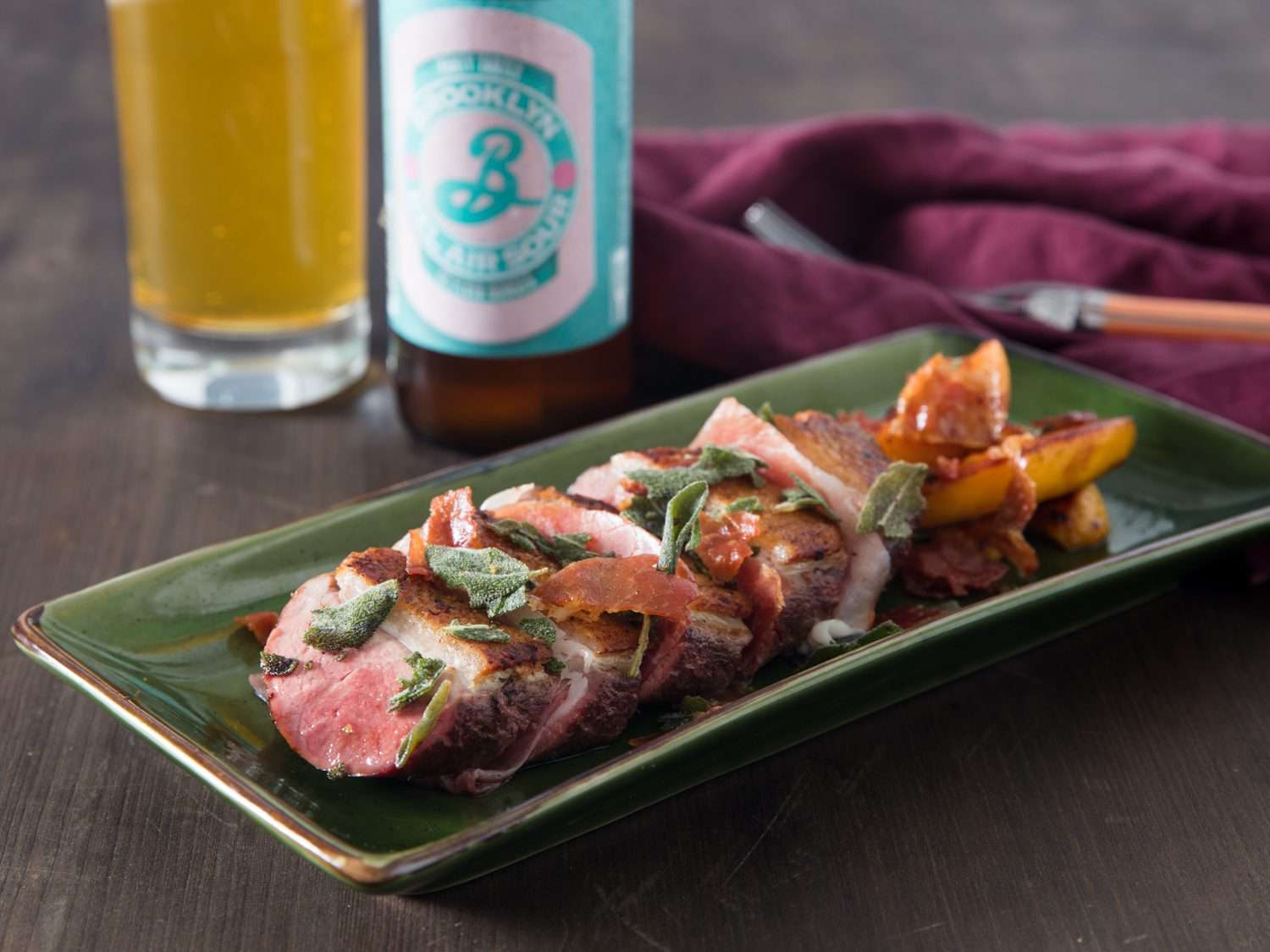 Plate of duck saltimbocca in front of glass and bottle of sour beer