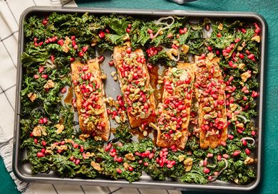 Salmon fillets topped with pomegranate seeds and greens on a baking sheet