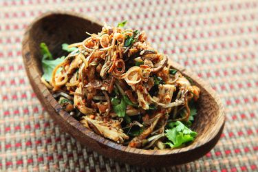 A wooden bowl filled with a flavorful Thai chicken, banana blossom, and herb salad.