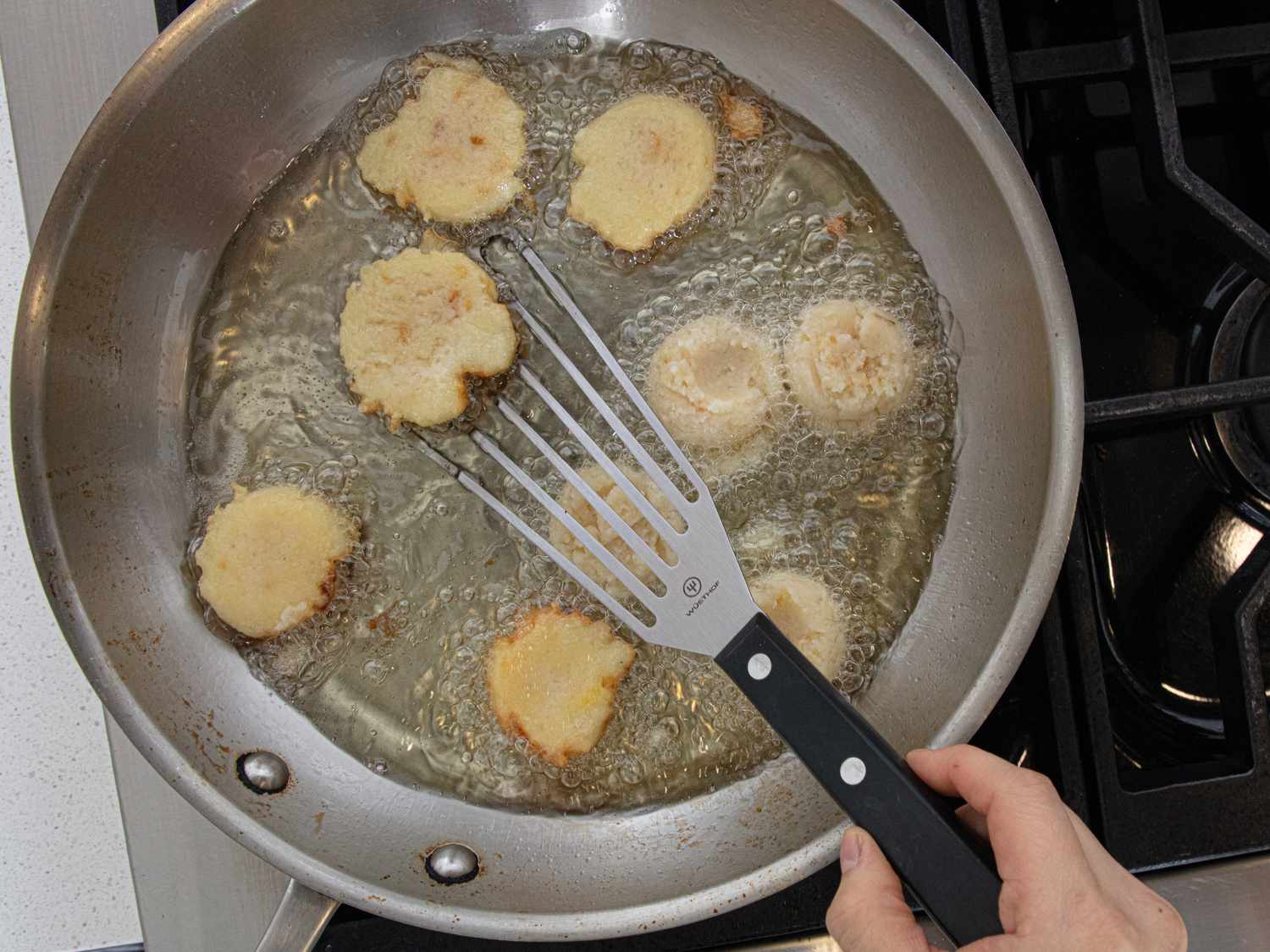 Latkes being fried in a skillet with a spatula holding one of them