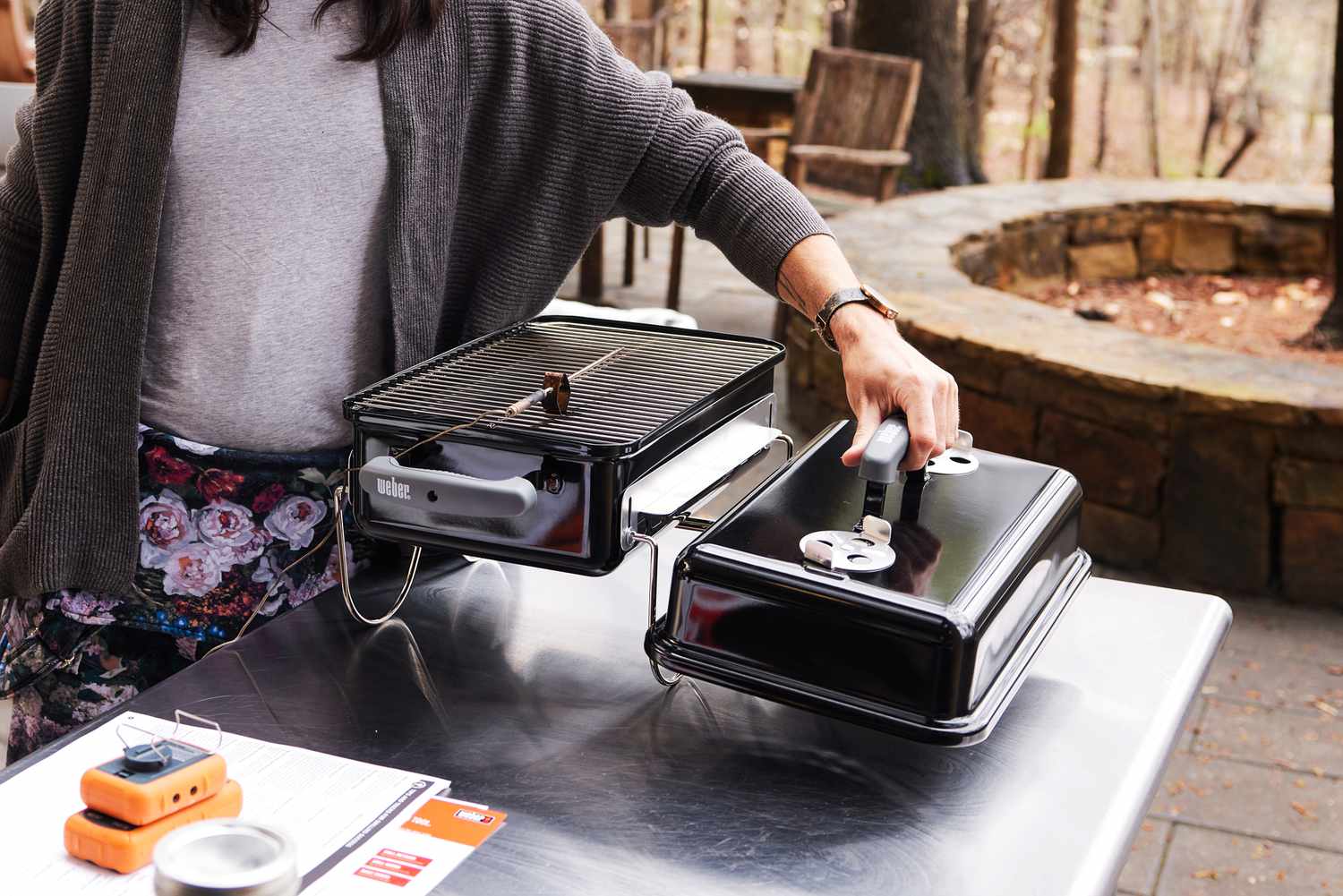 A person removing the lid from the Weber Go Anywhere charcoal grill.