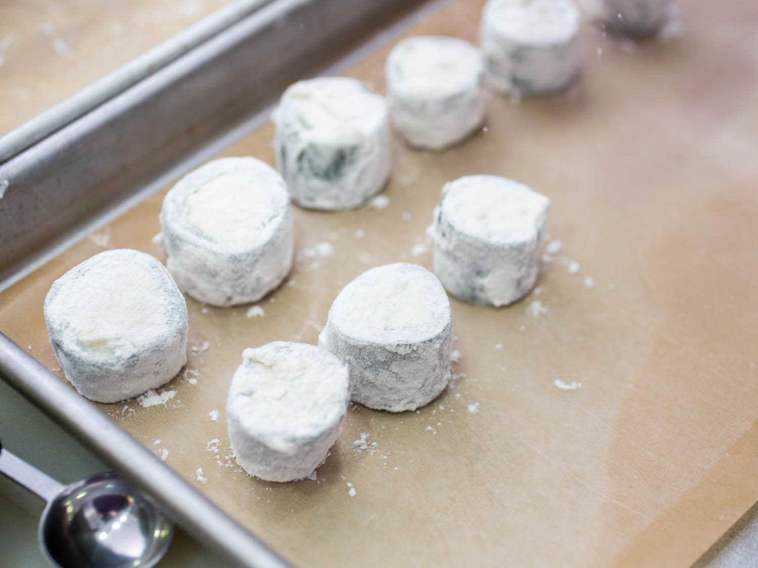 Filled and floured jalapeño rings lined up on a parchment-lined baking sheet.
