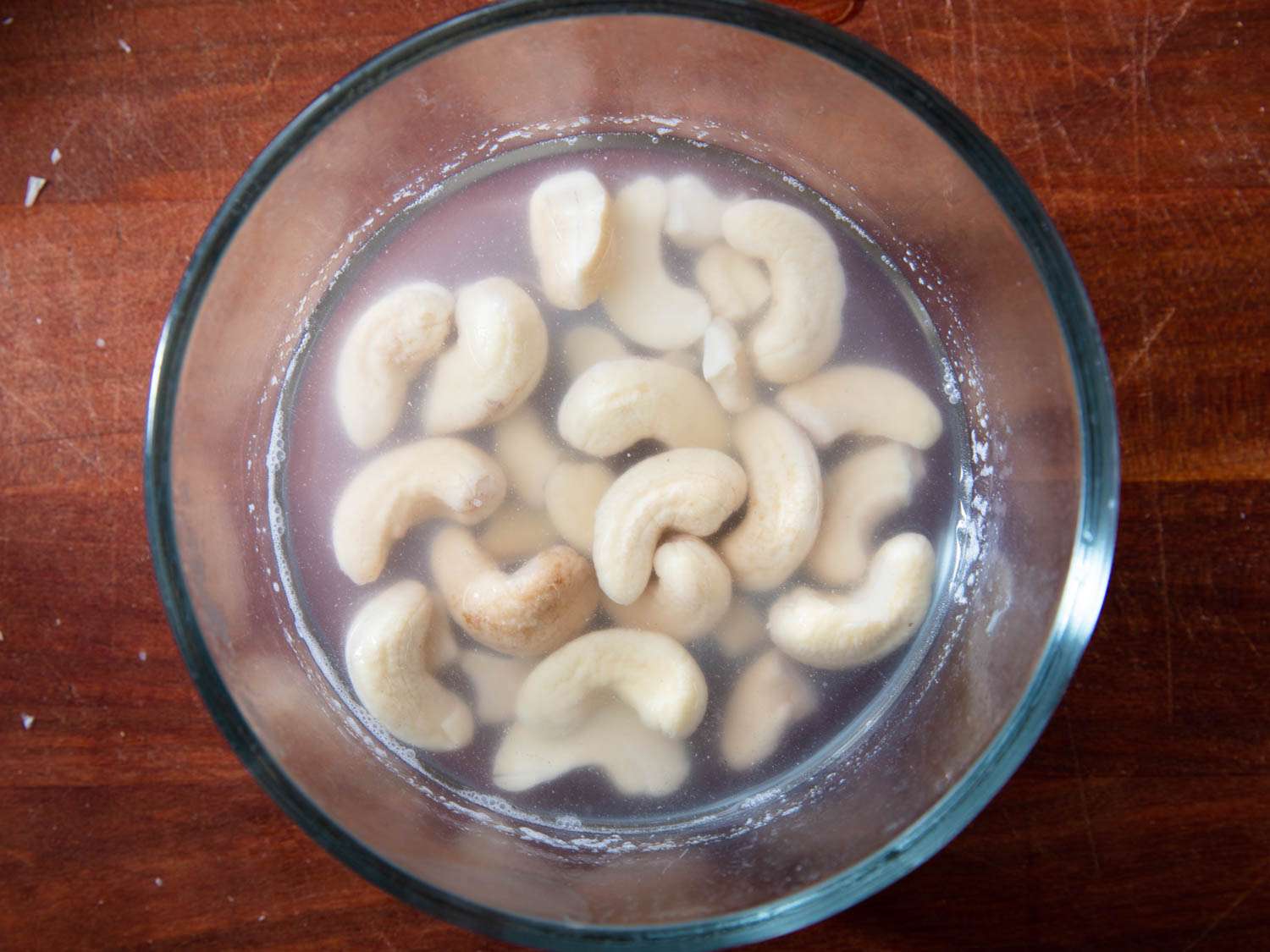 Overhead close-up of softened cashews submerged in water.