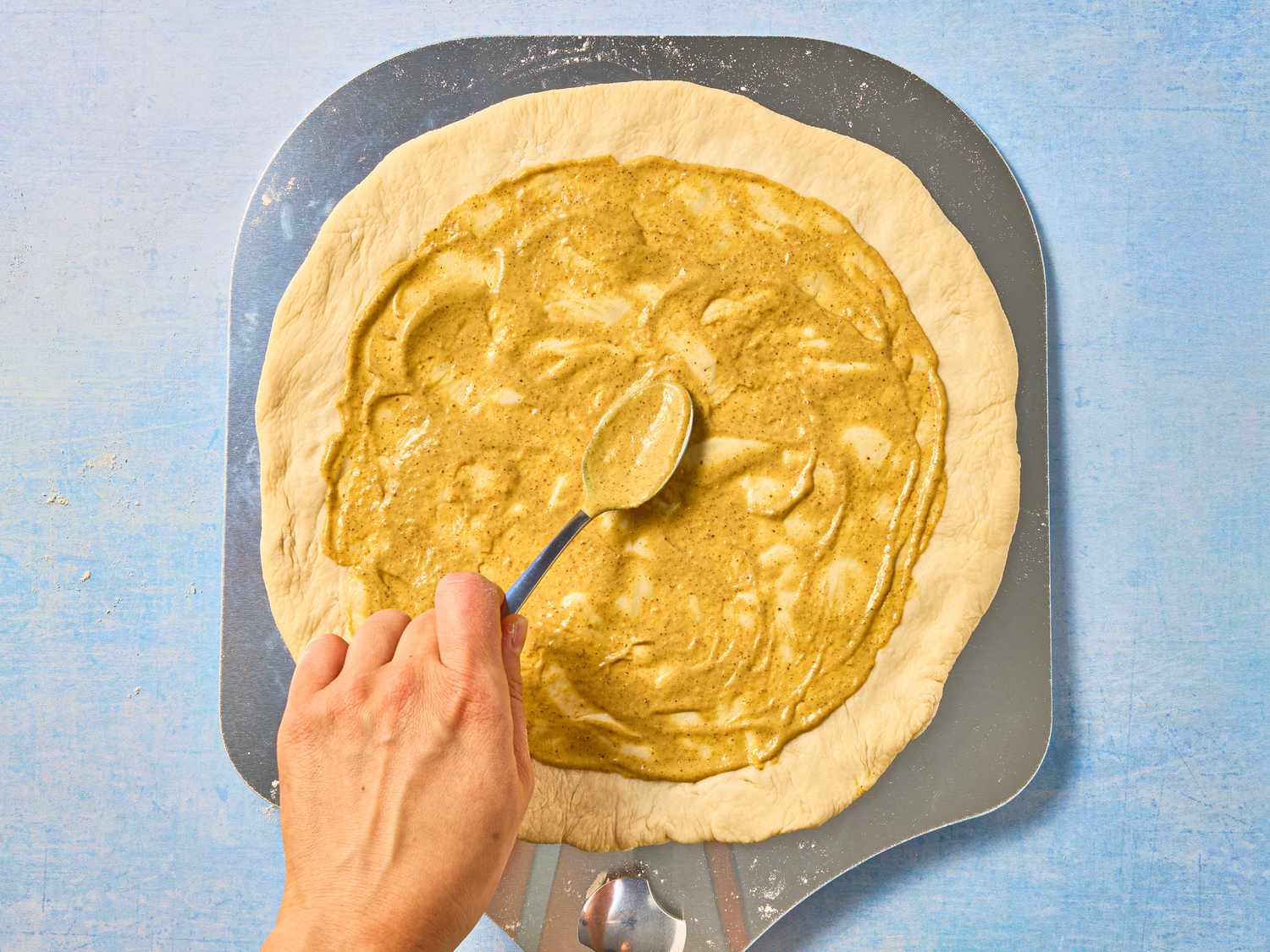 using a back of spoon to spread buster over pizza dough