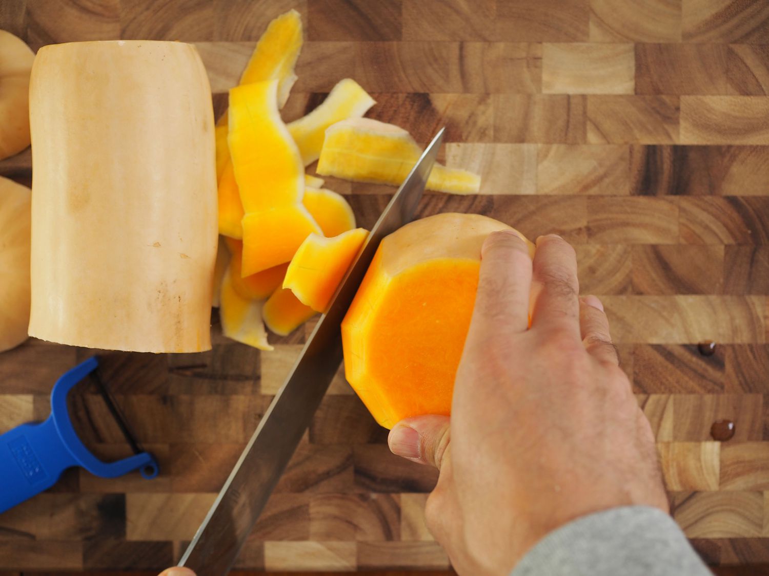 A knife trimming the hard, remaining pieces of skin off of the body of a butternut squash.