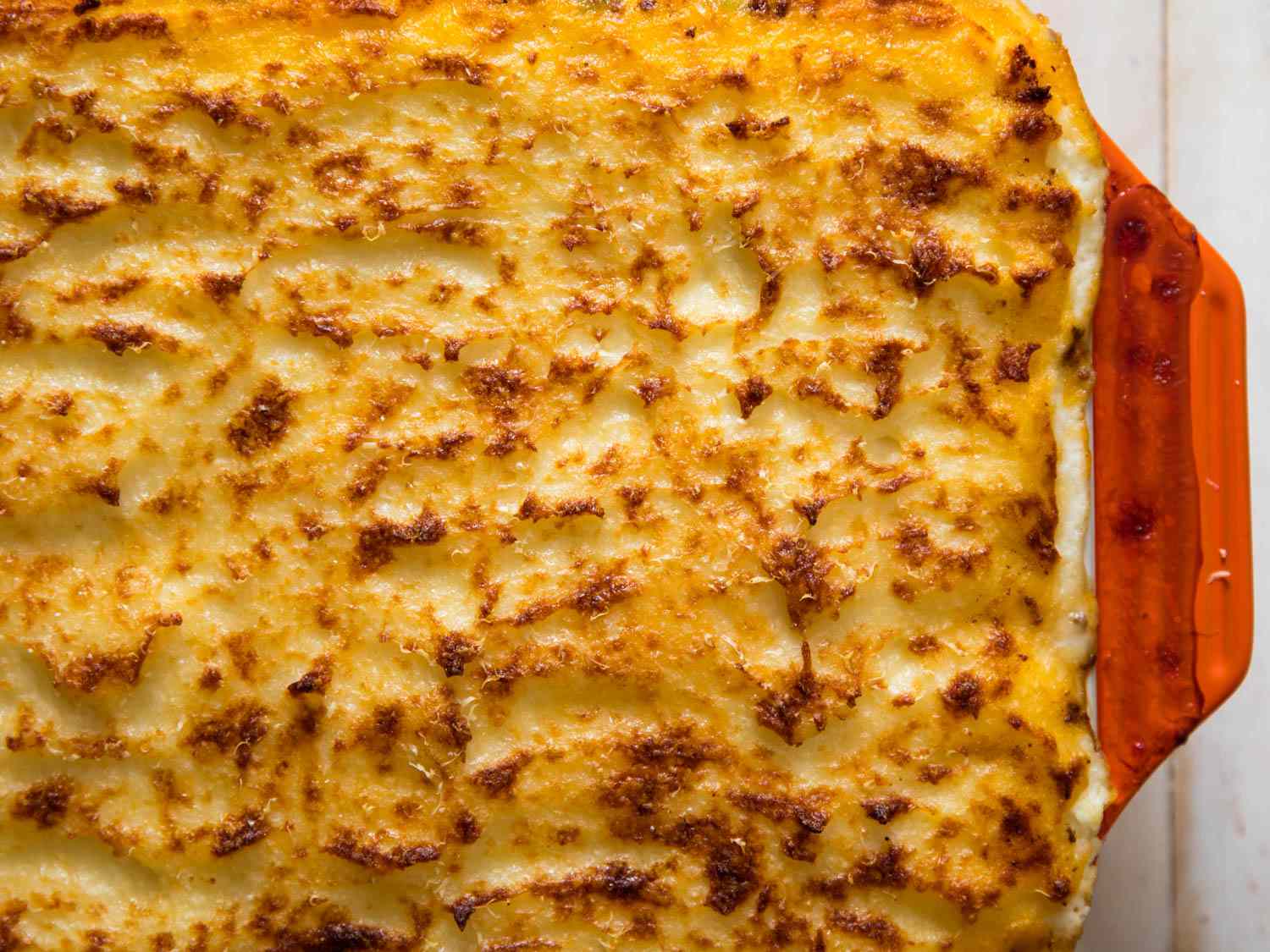 Overhead shot of golden mashed potato topping on shepherd's pie in red casserole dish. 