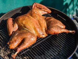 A spatchcocked turkey cooking on a grill. 