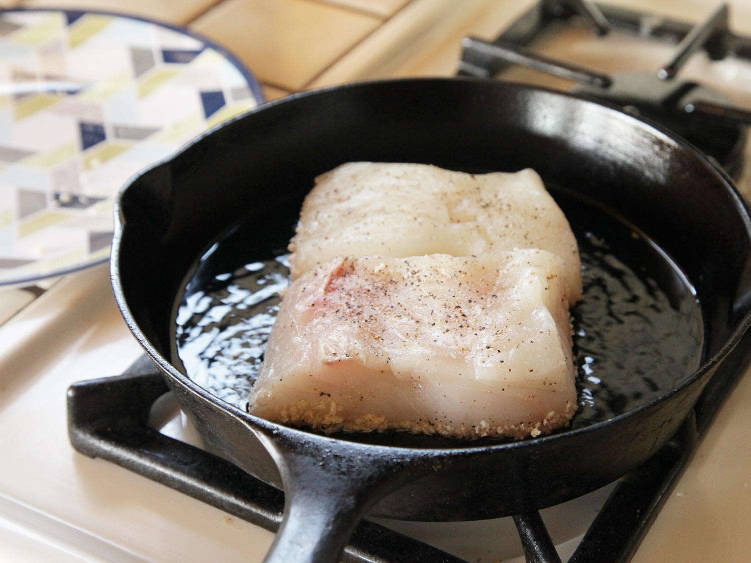 Fish fillets frying in a cast iron skillet.