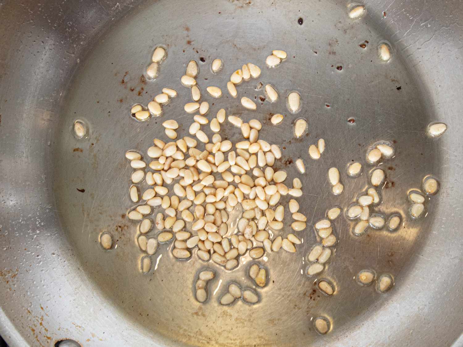 Pine nuts being toasted in a metal pan