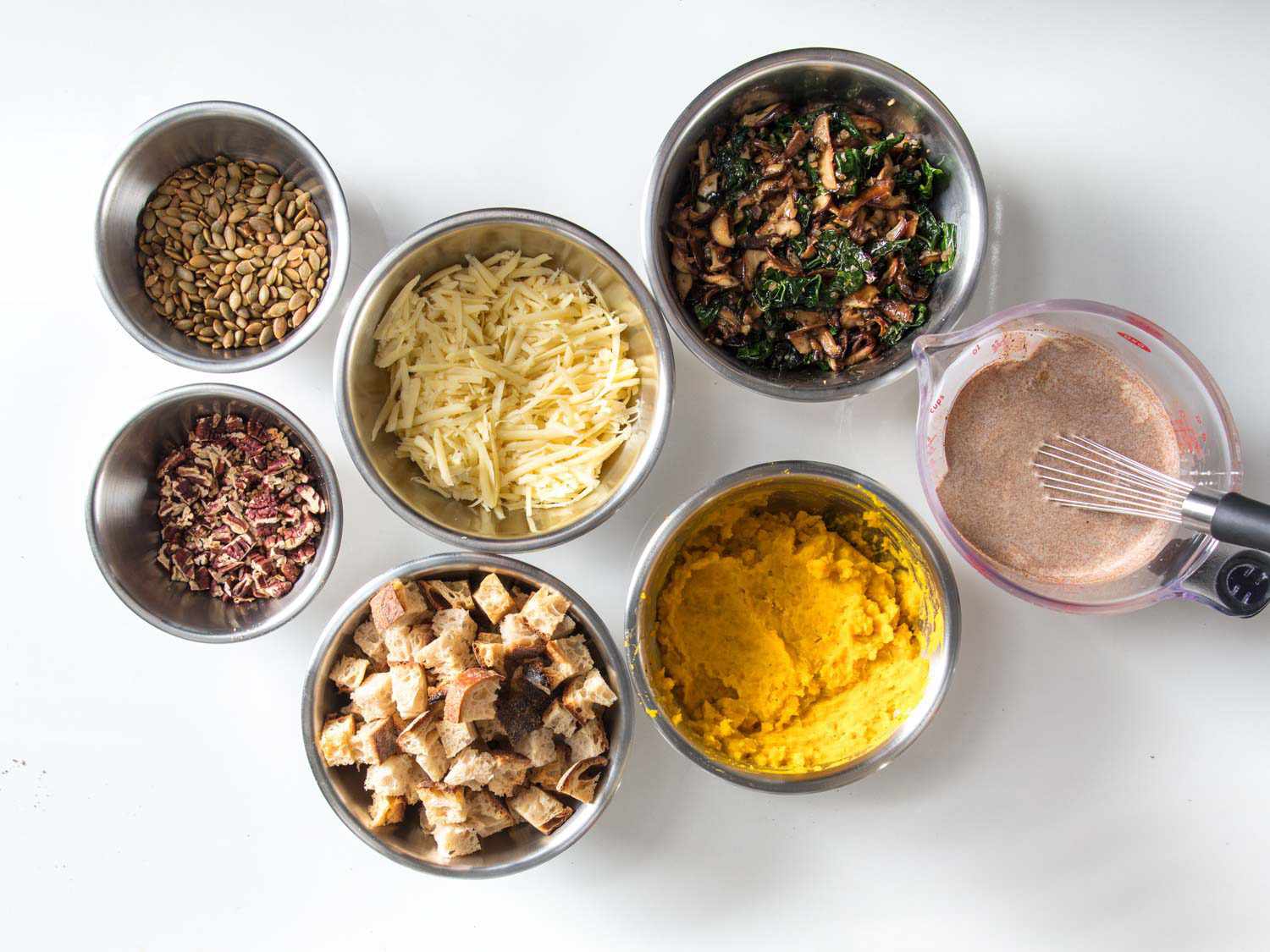 Mise en place showing bread, squash puree, pecans, Gruyere cheese, pepitas, kale, mushrooms, and spiced cream.